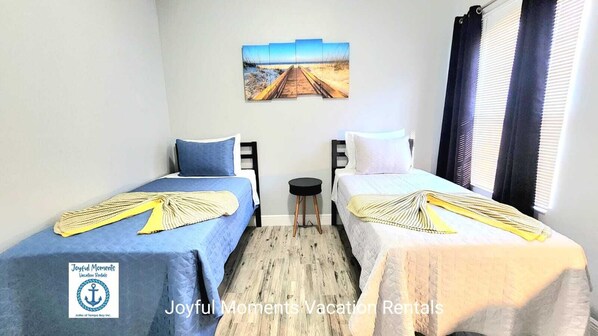 Une chambre avec deux lits, une petite table et un tableau au mur.