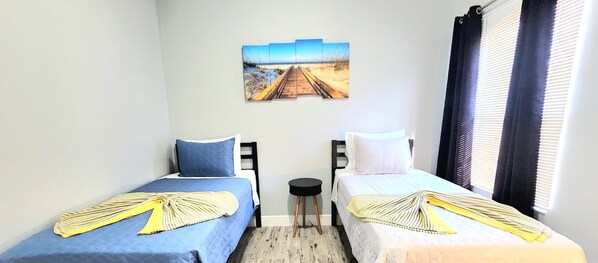 Ein Zimmer mit zwei Betten, einem kleinen Tisch und einem Bild an der Wand.