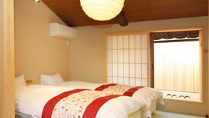 A room with two beds, a ceiling fan, an air conditioning unit, and a shoji screen window. - Sen Omiya-Gojo (Kyoto)