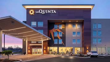 Un hôtel La Quinta au design moderne, avec un logo solaire bien visible, une entrée abritée et un espace de stationnement.