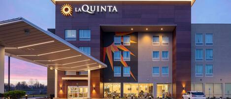 A La Quinta hotel with a modern design, featuring a prominent sun logo, a covered entrance, and a parking area.