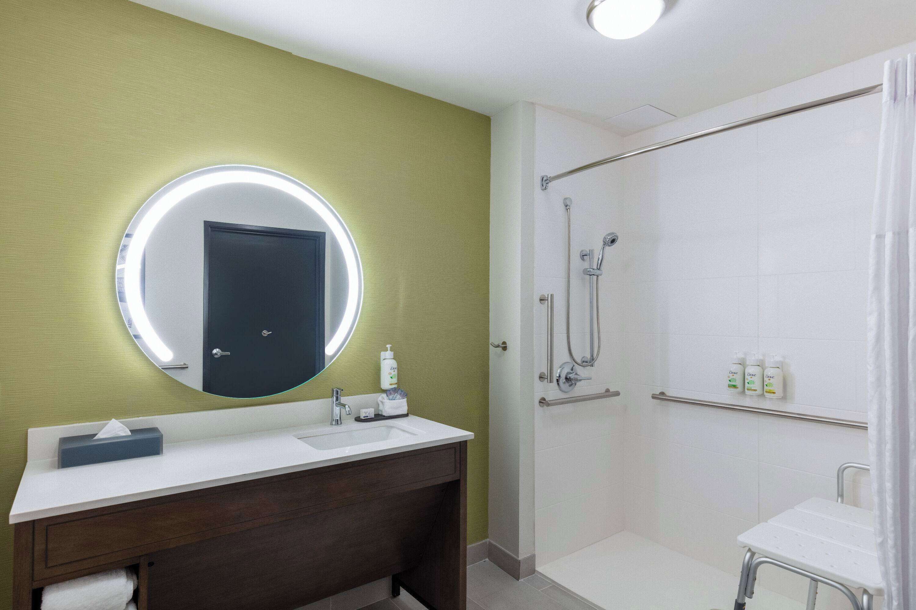 Un baño con un espejo redondo, un lavamanos y una ducha.