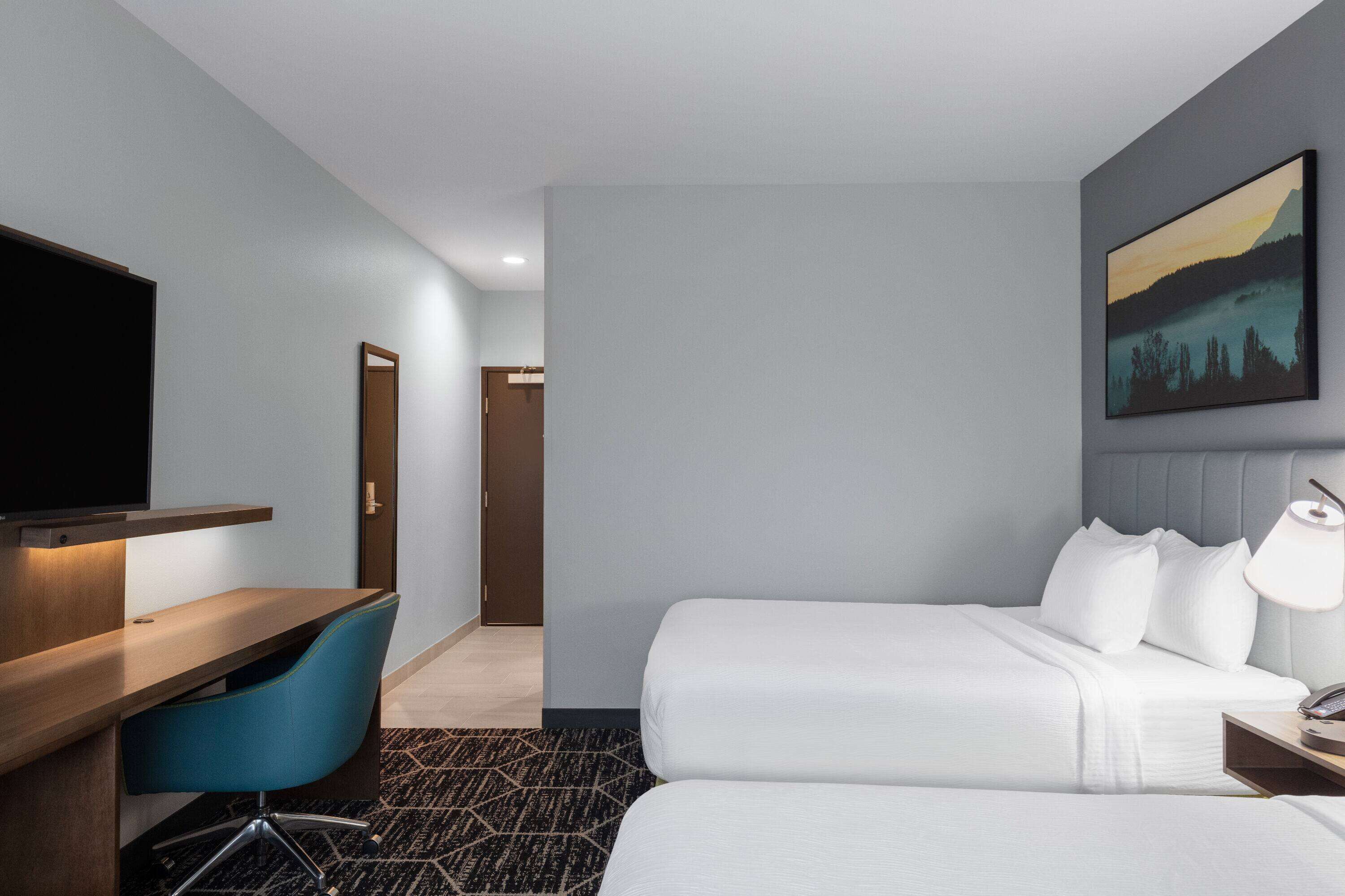 A hotel room with a bed, a desk with a chair, a TV, and a painting on the wall.