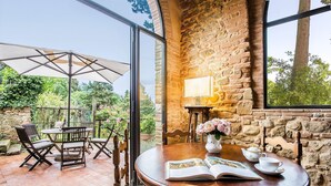 A cozy outdoor seating area with a round wooden table, chairs, and a glass enclosure.