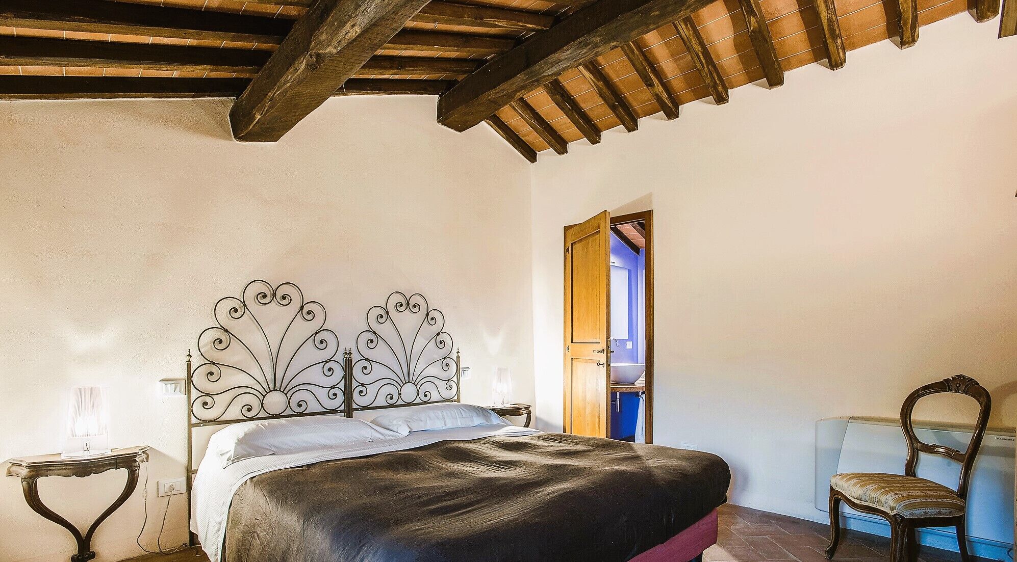 Un dormitorio con cama, mesita de noche, una silla y techo de madera.