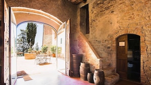 An interior with a stone wall, wooden door, and a view of an outdoor patio with tables and chairs. - Luxury, Sustainability and Eco Pool in Frangi Apt. (Certaldo)