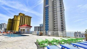 A rooftop pool area with lounge chairs and a view of high-rise buildings. - Breathtaking 2BR Condo w Floor-to-Ceiling Windows Overlooking Ocean (Myrtle Beach)
