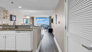 A modern kitchen with a dishwasher, a dining area with a view, and a hallway leading to a balcony. - Breathtaking 2BR Condo w Floor-to-Ceiling Windows Overlooking Ocean (Myrtle Beach)