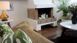 Ein gemütlicher Wohnraum mit Kamin aus Backsteinen, einem Korbsessel und einem runden Tisch sowie einer Lampe.