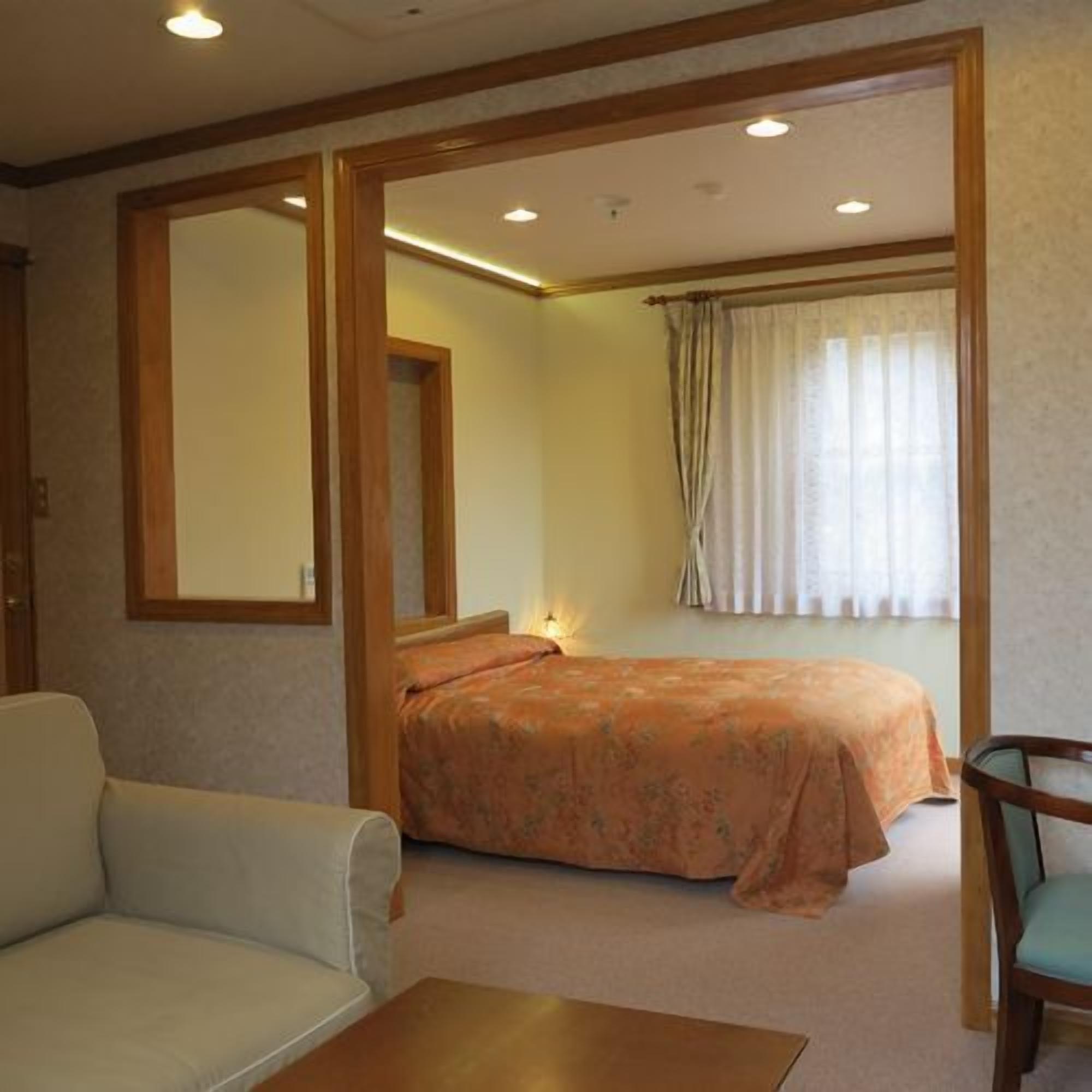 Quarto com cama, poltrona, sofá e mesa pequena.