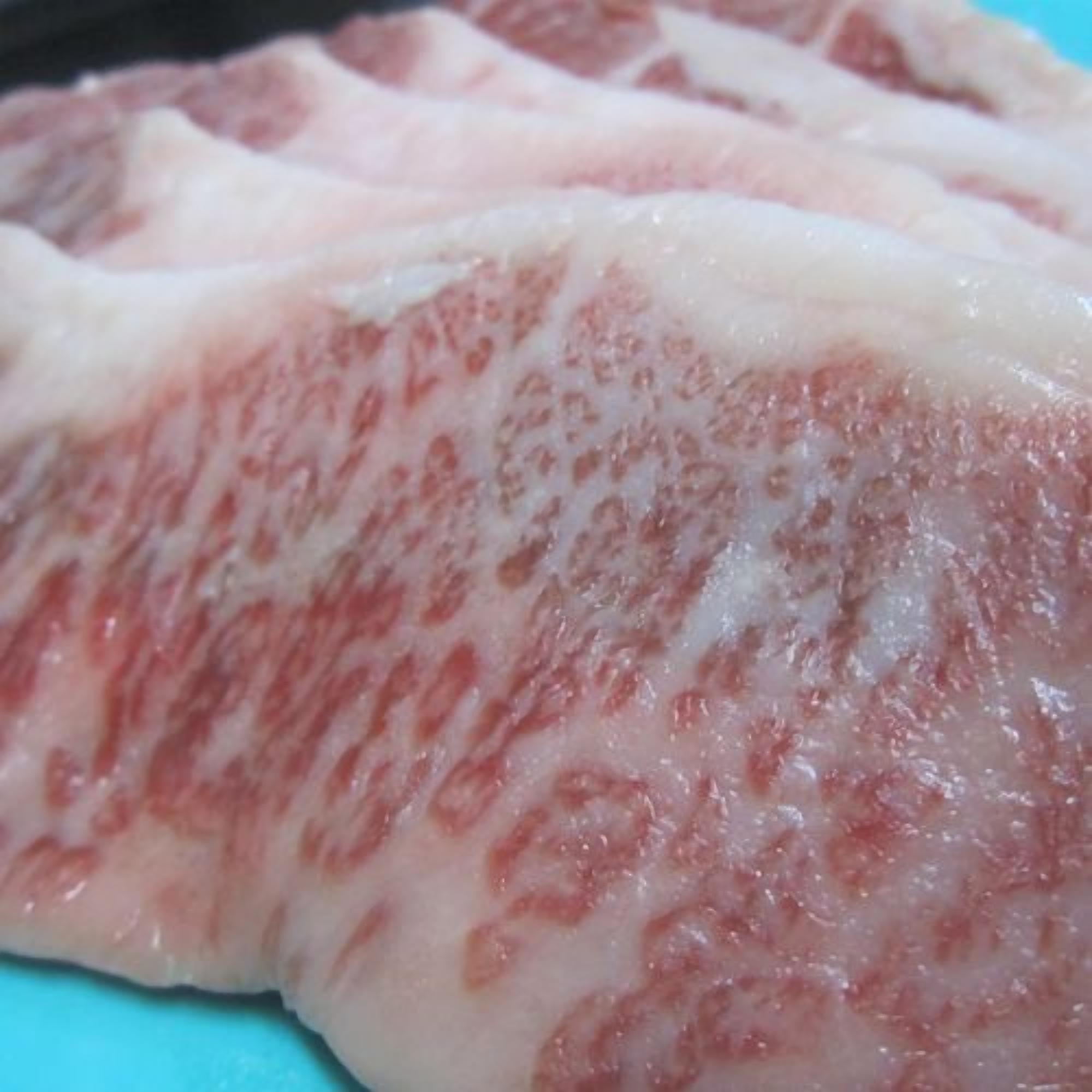 Primer plano de carne cruda con tonos rosados y vetas de grasa visibles.