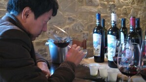 Une personne assise à une table, devant des bouteilles de vin et des verres.