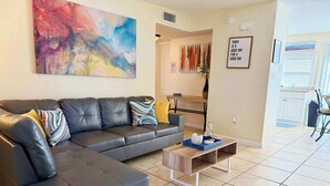 A modern living room with a sectional sofa, a coffee table, and a colorful abstract painting on the wall. - Close to the beach ~ Pool, gym, BBQ, pet-friendly (Indian Harbour Beach)