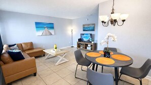 Un salon comprenant un canapé, une table basse, un téléviseur, une table à manger avec des chaises et un lustre.