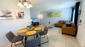 Een moderne woonkamer met een bank, een eettafel met stoelen, en kunstwerken aan de wanden.