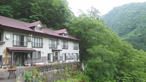 A two-story building with a red roof, surrounded by lush greenery and hills.
