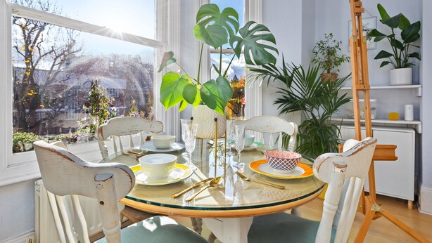 A dining area with a round glass table, white chairs, and a wooden easel.