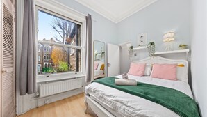 A bedroom with a large window, a bed with white and green bedding, a dresser, and a mirror.