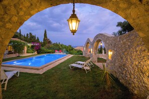 A swimming pool with stone walls and arches, surrounded by grass and plants.