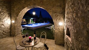 Eine Terrasse im Freien mit Steinmauern, einem Pool, einem Tisch mit Stühlen und einer Weinflasche.