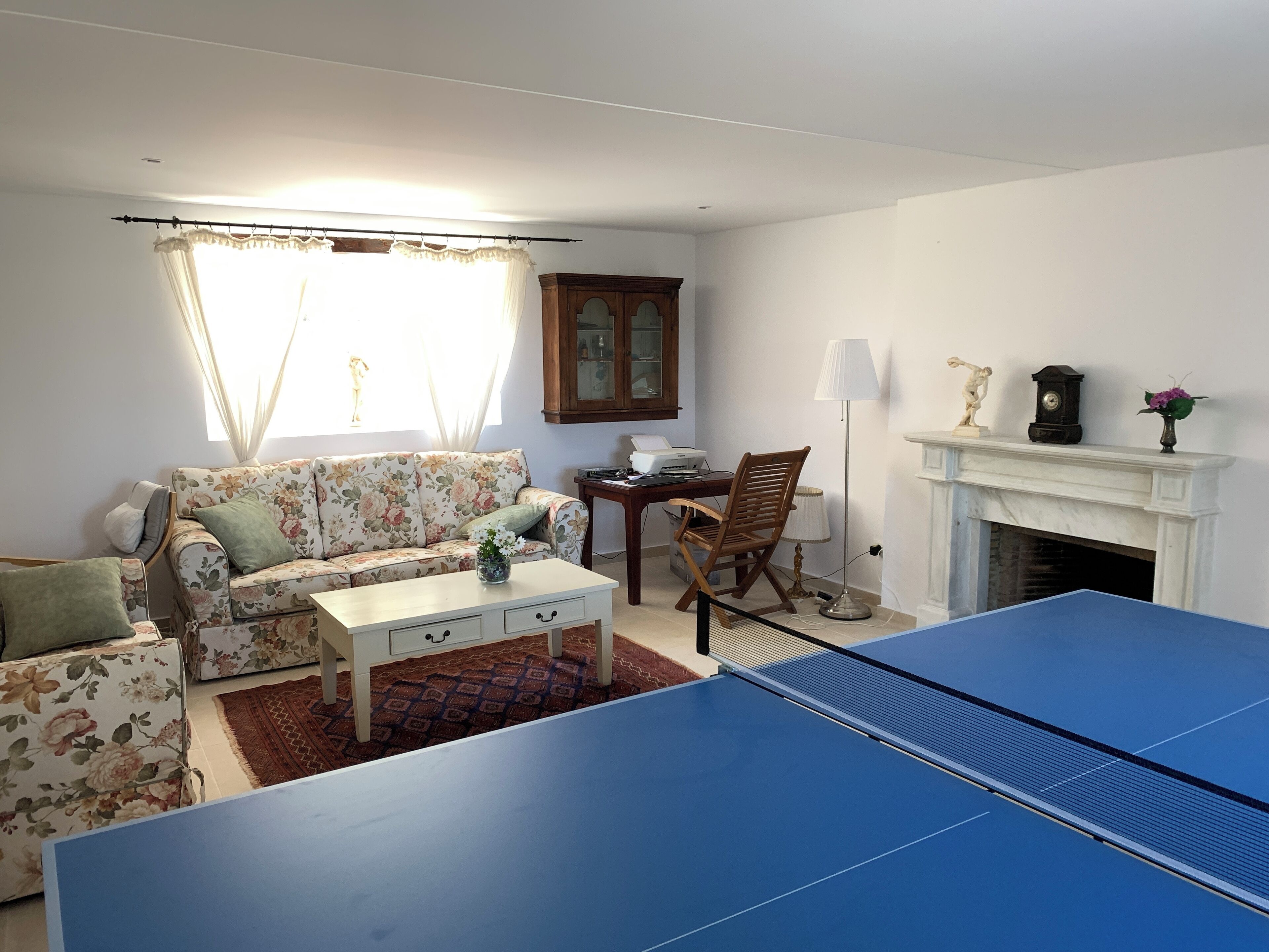 Un salon avec une table de ping-pong, un canapé à motifs floraux et une cheminée.