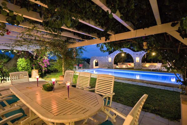 An outdoor patio with a pool, surrounded by greenery and stone structures.