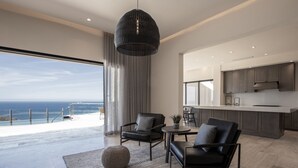 Un salon moderne doté d’une grande fenêtre donnant sur un balcon, d’un coin cuisine et d’un espace repas.