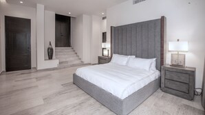 Une chambre moderne avec un grand lit, une table de chevet, une lampe et un escalier menant à une autre pièce.