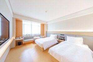 Habitación de hotel con dos camas, una ventana con cortinas, una mesita y un televisor en la pared izquierda.