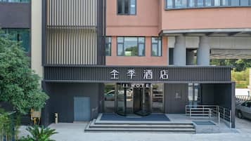 Entrada de hotel com porta giratória, área de estacionamento para carros visível e vista clara da fachada do edifício.