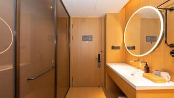 A modern hotel bathroom with a glass shower enclosure, a wooden vanity with a mirror, and a white countertop.