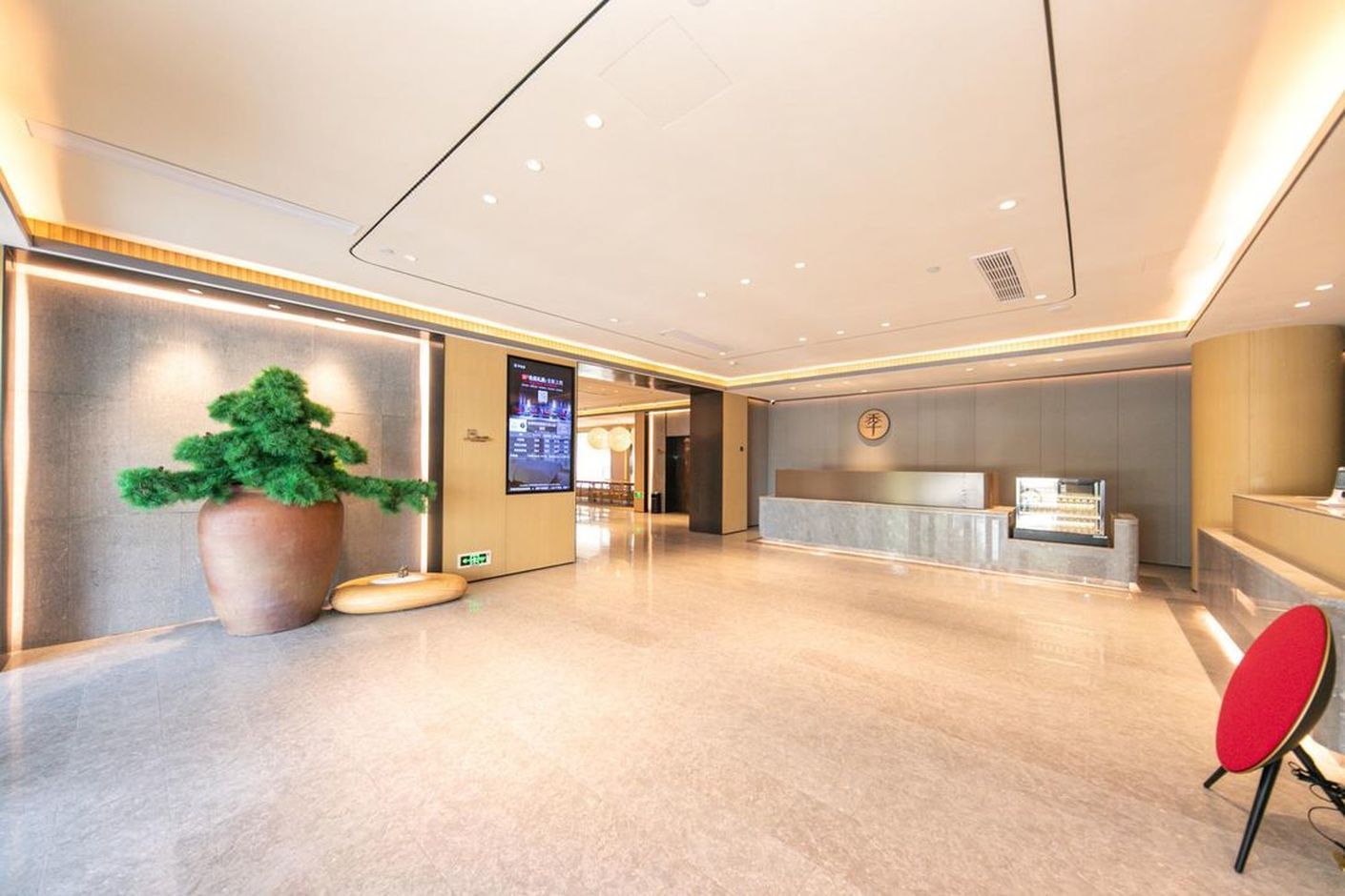 A modern hotel lobby with a reception desk, a large potted plant, and a digital information screen.