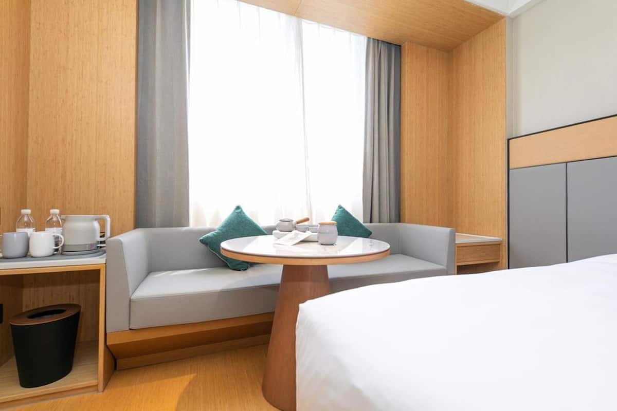 Habitación de hotel con cama, una mesa redonda, un sofá, una mesita de noche y una ventana con cortinas.