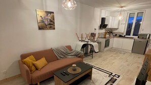 A modern living room with a sofa, coffee table, and a television. There is a kitchen area with a microwave and a sink. - Cosy apartment (Villemurlin)