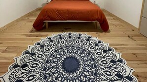 A bedroom with a bed, a hanging light fixture, a wooden slat headboard, and a patterned rug. - Cosy apartment (Villemurlin)