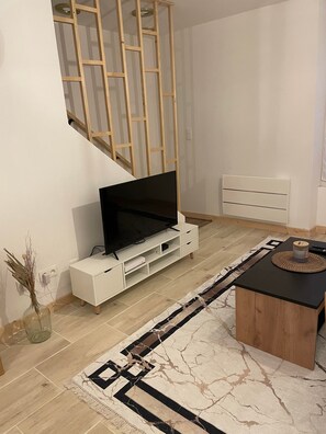 En moderne stue med et fladskærms-tv på et hvidt tv-møbel, et træ sofabord og en tæppe med et mønster.