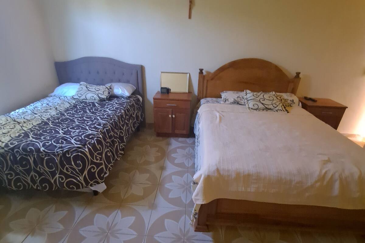 Een kamer met twee bedden, een nachtkastje, een klein kastje en een kruis aan de muur.