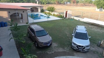 Un barrio residencial con dos coches aparcados en el césped, una piscina y una casa con techo rojo.