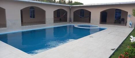 A rectangular swimming pool with a curved section, surrounded by a light-colored tiled deck.
