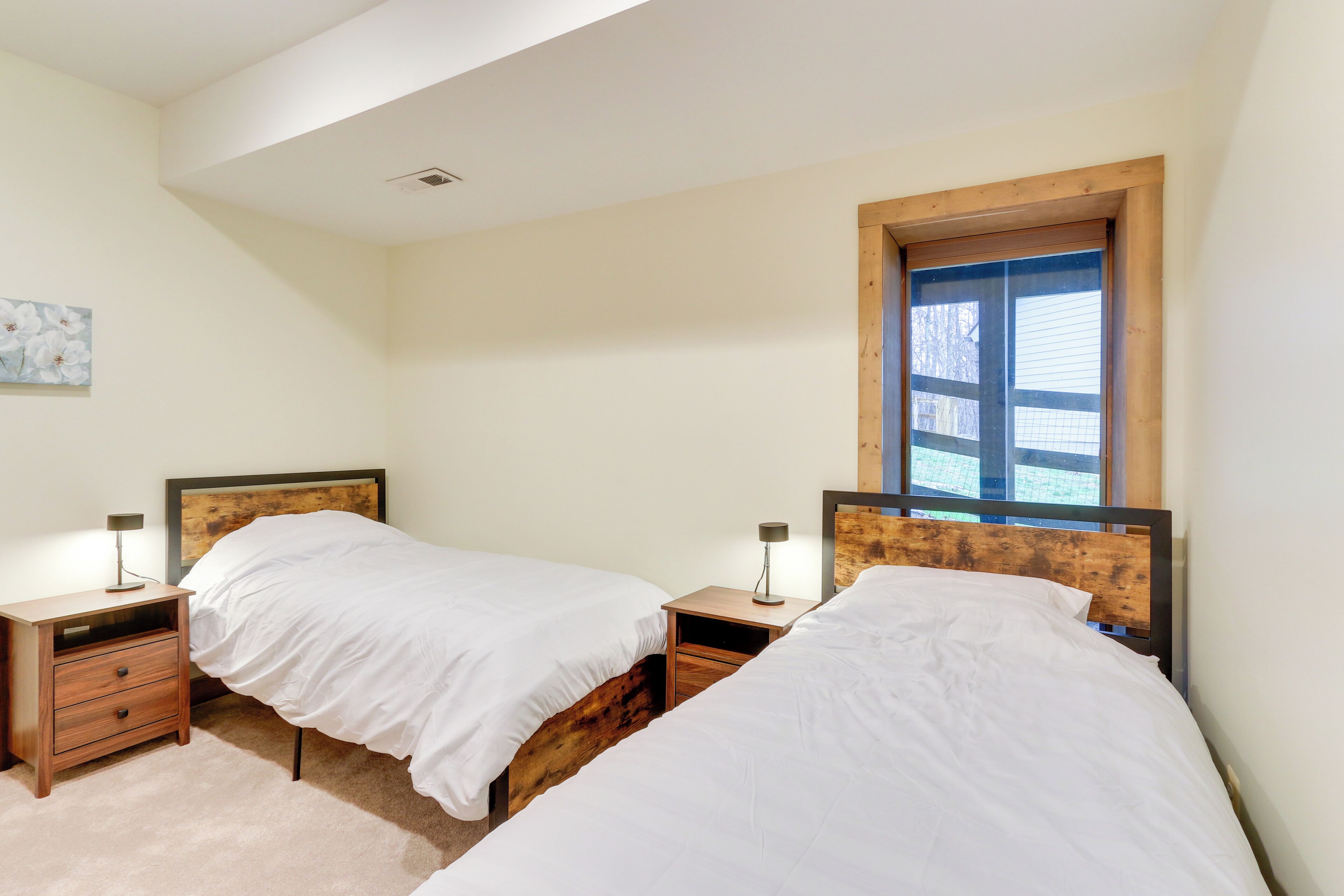 Une chambre avec deux lits simples, des têtes de lit en bois, des tables de chevet avec des lampes et une fenêtre avec des stores.
