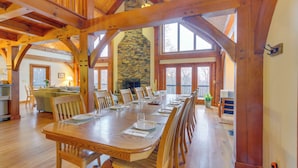 A spacious dining area with a long wooden table set for a meal, surrounded by wooden chairs. A stone fireplace is visible in the background, and the room features high ceilings with exposed wooden beams. - Spacious Virginia Vacation Rental w/ Yard & Sauna (Purcellville)