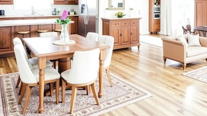 A modern kitchen with wooden cabinets, a stainless steel refrigerator, and a dining area with a wooden table and white chairs. - Remodeled House with Pool on Quiet cul-de-sac!  Walk to beach on Bay! (Shalimar)