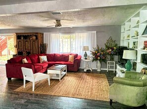 Un salon avec un canapé rouge, un fauteuil blanc et un fauteuil vert, une table basse et une bibliothèque.