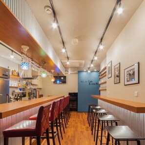 A bar area with wooden bar tops, red cushioned chairs, and hanging colorful light fixtures. - Asta Hotel (Tokyo)