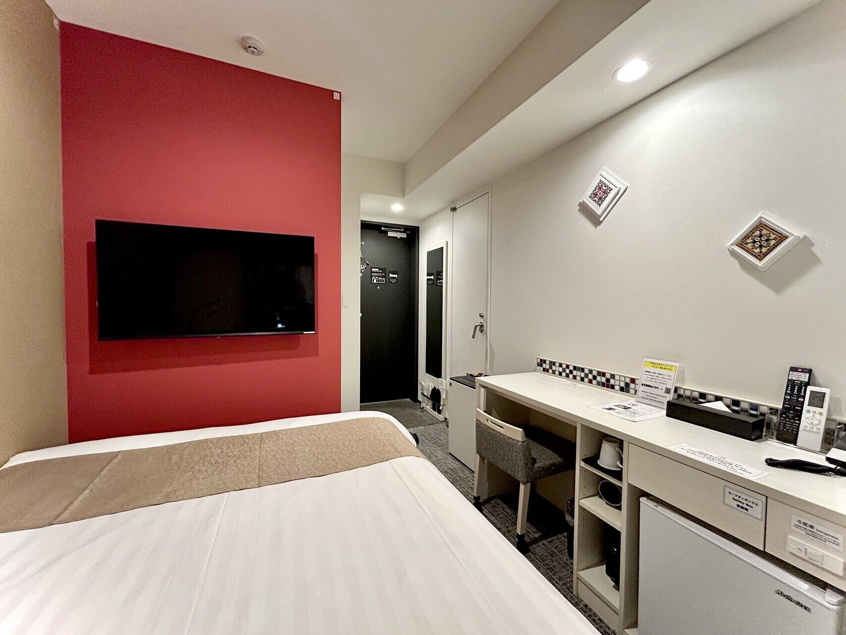 A hotel room with a bed, a desk with a computer, a TV, and a small refrigerator.