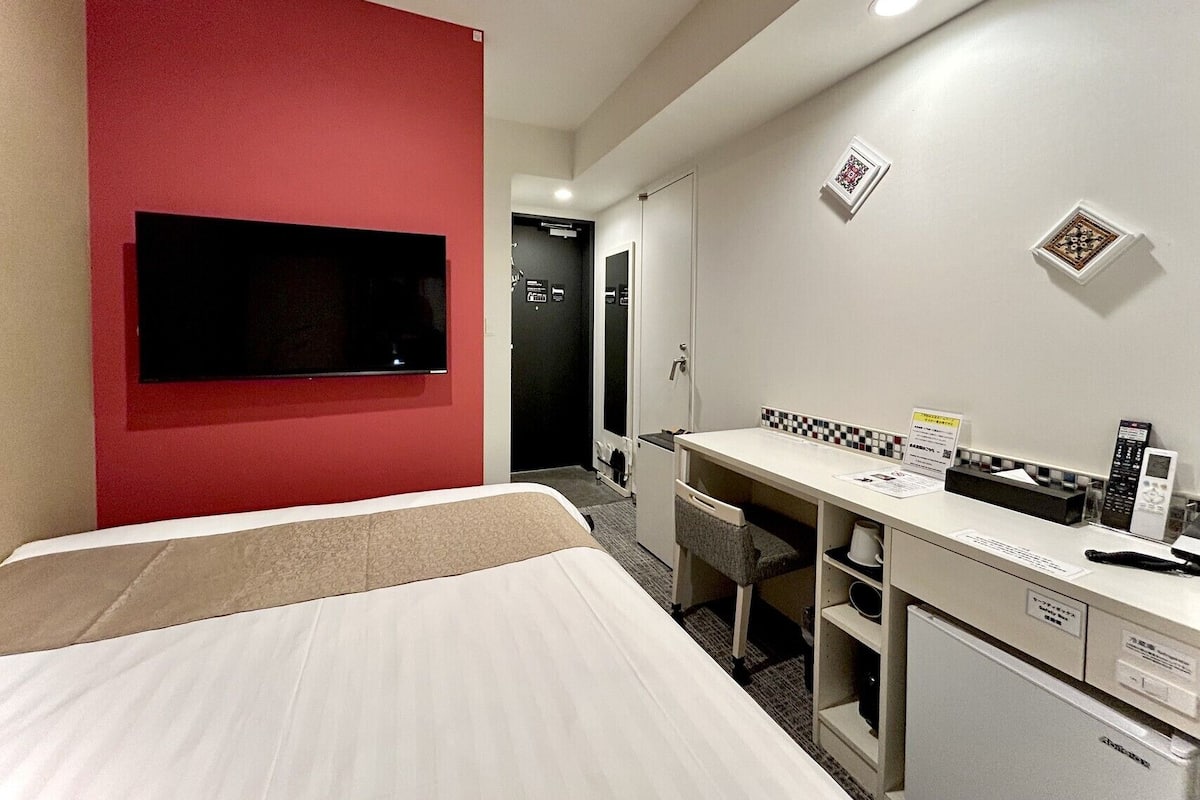 A hotel room with a bed, a desk with a computer, a TV, and a small refrigerator.