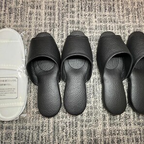 Schwarze Hausschuhe und ein Behälter aus Plastik mit Aufschrift auf einem strukturierten Teppich.