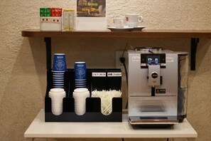 A coffee station with a coffee machine, milk and sugar dispensers, and stacked cups.