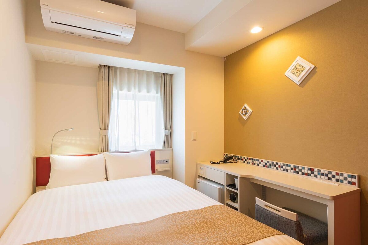 Ein Hotelzimmer mit einem Bett, einem Schreibtisch, einer Klimaanlage und einem fenster mit Vorhängen.