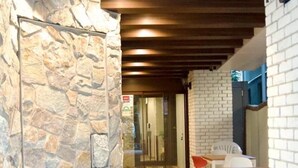 A hallway with a stone wall, a wooden ceiling, and a glass door leading to a room. There are chairs and a table in the hallway. - Asta Hotel (Tokyo)